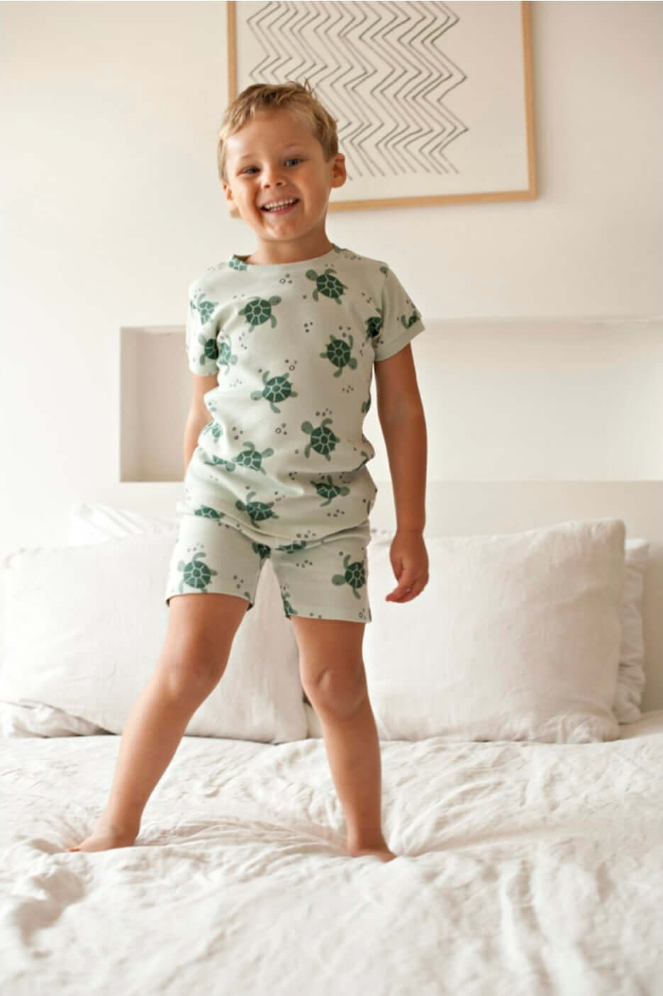 Kind in Feetje premium zomermode Timmy Turtle op bed met groene zeeschildpaddenprint.